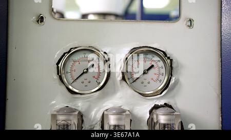 A close up of two industrial pressure gauges on a white control panel. The manometers measure pressure in bar and psi, showing readings on a white, re Stock Photo