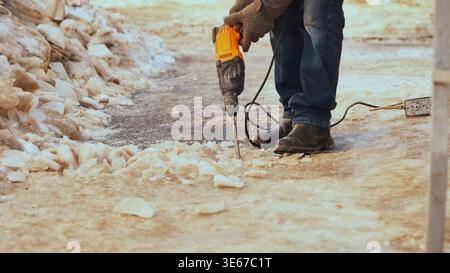 Worker using jackhammer to remove ice from a snow-covered sidewalk during winter Stock Photo