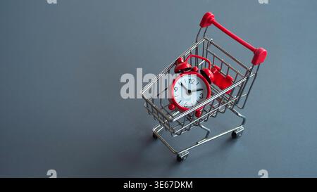 Red alarm clock placed inside a small silver shopping cart representing time-sensitive deals, limited time offers, and fast delivery service. Stock Photo