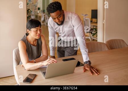 Two professionals discussing project over laptop at desk during office meeting, focused on teamwork and success Stock Photo