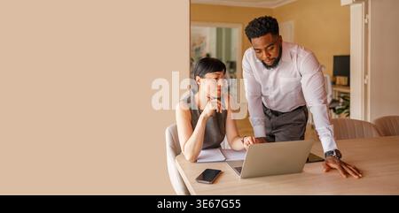 Confident professional colleagues discussing project strategies over laptop while collaborating at desk in office Stock Photo