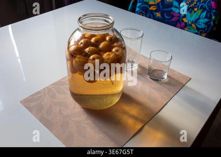 Large glass jar filled with homemade apple compote or pickled apples on a brown placemat in a sunlit kitchen Stock Photo