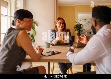 Confident businesswoman in eyeglasses explaining project strategies to colleagues during office meeting Stock Photo