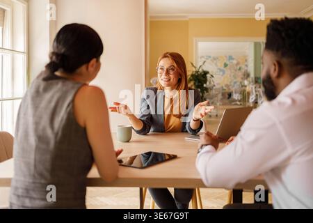 Confident businesswoman in eyeglasses discussing project plans with colleagues during collaborative meeting Stock Photo