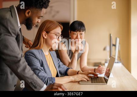 Diverse team of professionals analyzing financial report on laptop while collaborating in business meeting Stock Photo