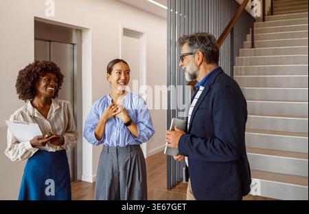 Male lawyer holding laptop discussing legal strategies with female colleagues while standing together in modern office Stock Photo