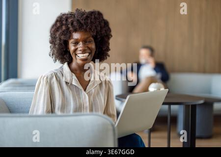 Portrait of smiling female accountant analyzing financial report over laptop while sitting on sofa in corporate office Stock Photo