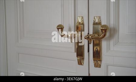 Classic art deco style brass handles adorning elegant white double doors, featuring intricate fan and knob details Stock Photo