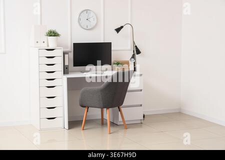 Workplace with computer, lamp and clock on light wall in office Stock Photo