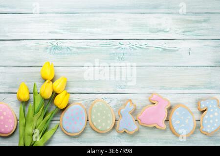 Easter gingerbread cookies and tulips on wooden table. Eggs and rabbits. Top view with space for your greetings Stock Photo