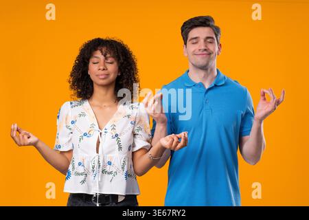 Calm interracial Couple Relaxing, Meditating, Refuses Stress. Man And Woman Breathes Deeply with mudra om on yellow studio background. High quality Stock Photo
