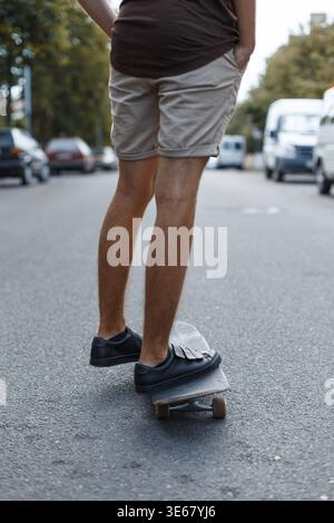 A young guy in summer clothes rides a skateboard on the street Stock Photo