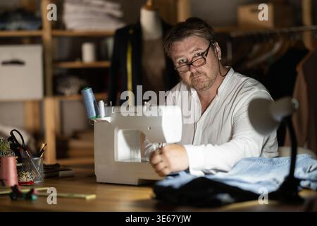 Middle-aged male dressmaker working with sewing-machine at night Stock Photo