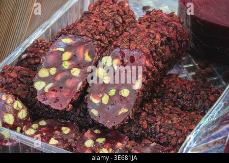 Rich, dark chocolate treats with visible pistachios and fruit pieces. The sweets are arranged in a clear plastic container. They show a textured, chun Stock Photo