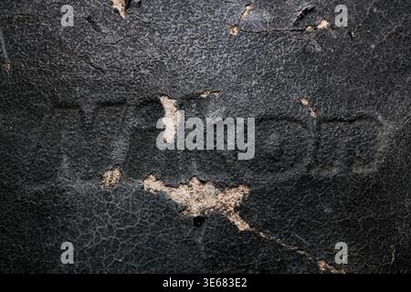 Close-up of cracked, worn black leather with faint embossed letters and areas where surface flaked away revealing lighter material beneath Stock Photo
