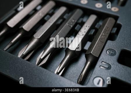 Close-up of metal screwdriver bits arranged in a foam tray, sharp focus on tips and hex shanks, cool-toned industrial lighting Stock Photo