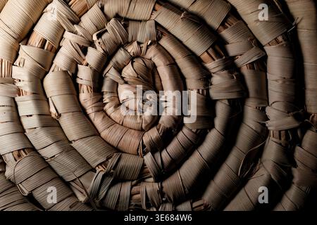 Close-up spiral of woven dried palm or straw fibers forming a rustic coiled mat with textured, overlapping strips in warm brown tones Stock Photo