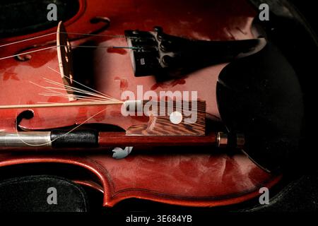 Close-up of a violin and bow resting inside a case, warm reddish wood grain, bow horsehair fibers visible, moody low-light music still life Stock Photo