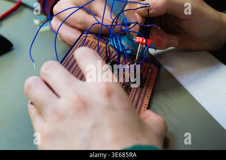 Hands are soldering a breadboard with blue wires using a soldering iron. Stock Photo