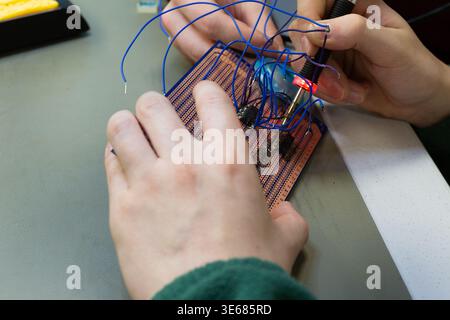 Hands are soldering a breadboard with blue wires using a soldering iron. Stock Photo