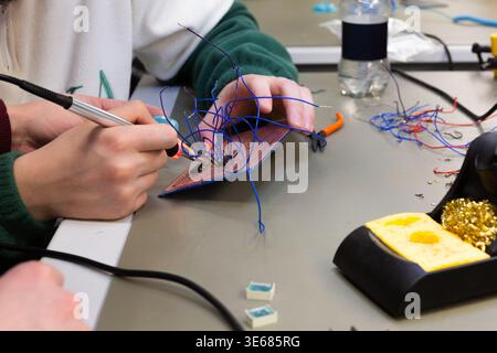 Hands are holding a soldering iron, working on a circuit board with numerous blue wires. Stock Photo