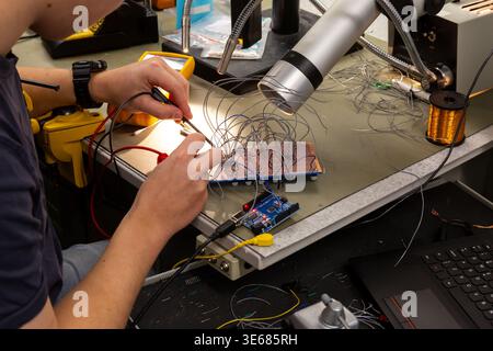 Closeup of hands holding a multimeter probe to a board with wires on it Stock Photo