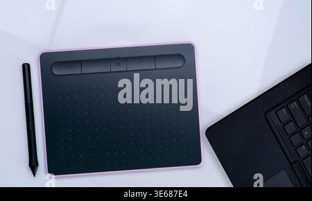 Digital drawing tablet with stylus beside laptop on white desk, showing how designers and artists work in modern offices using creative technology for Stock Photo