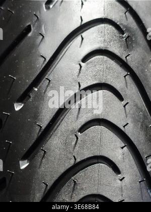 High-resolution macro shot of a brand-new automotive tire tread, featuring the intricate rubber texture, drainage grooves, and manufacturing vent spew Stock Photo