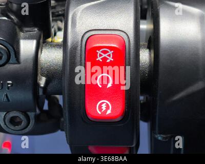 A detailed close-up shot of a red motorcycle engine kill switch and starter button mounted on a black handlebar. Essential safety control for ignition Stock Photo