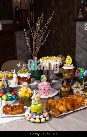 Richly decorated Easter table featuring traditional kulichi with white glaze and colorful toppings, fresh pastries, chocolate eggs, meringues and cute Stock Photo