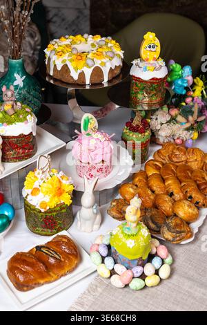 Luxurious Easter spread multiple kulichi in patterned molds with floral icing, wreaths of painted eggs, porcelain bunnies, pastries, candies, and flor Stock Photo