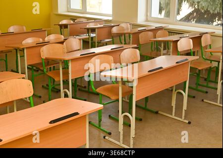 Classroom with rows of wooden desks and chairs in empty school interior, classroom space filled with natural light from large windows, education envir Stock Photo