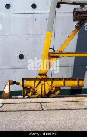 A vertical, high-angle shot focusing on the heavy industrial wheel assembly and the base of a bright yellow dockside crane. The weathered metal shows Stock Photo