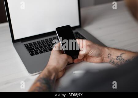 Professional male worker sitting in office with laptop and using smartphone Stock Photo
