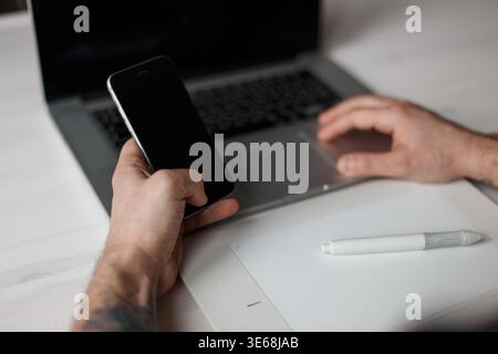 Professional designer man sitting at home at work desk with tablet and using smartphone Stock Photo