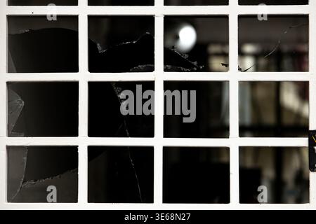Close-up of window with grid frame and broken glass panes, visible cracks and shattered sections. Concept of vandalism, neglect, security issues and u Stock Photo
