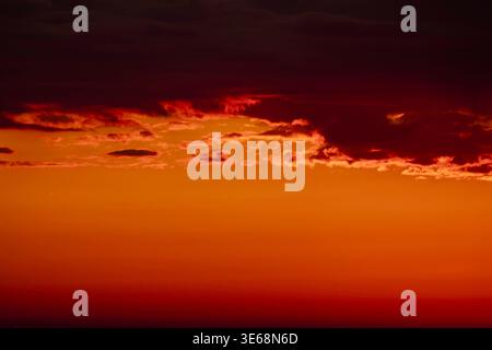 Dramatic red and orange sky with dark clouds illuminated by sunset light. Intense gradient colors and abstract cloud formations create a powerful atmo Stock Photo