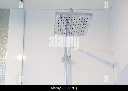 Modern bathroom fixture interior with square chrome rain showerhead with water falling in white bathroom Stock Photo