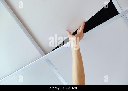 Technician service hand pushing ceiling tile upward for inspection, repair or maintenance inside residential Stock Photo