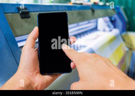 Closeup hand interacting with mobile phone and industrail inkjet printer for signage or large scale printing tasks Stock Photo