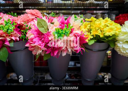 Assorted colorful artificial flower bouquets in grey pots on a store display. Bright pink, yellow, and red decorative flowers. Stock Photo
