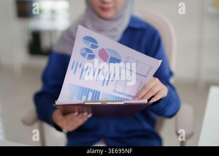 Adult Asian woman reviewing important financial data analysis statistics presented on a document with charts and graphs Business professional evaluati Stock Photo