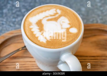 Cup of cappuccino with detailed latte art in shape of monkey on milk foam served on wooden tray. Close up. Coffee beverage and barista design Stock Photo