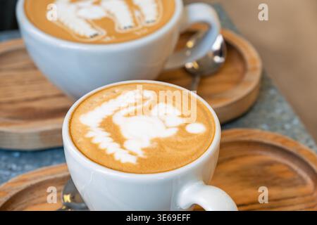 Two cups of cappuccino with latte art in shape of animals on milk foam served on wooden tray. Close up. Coffee beverage and barista design Stock Photo
