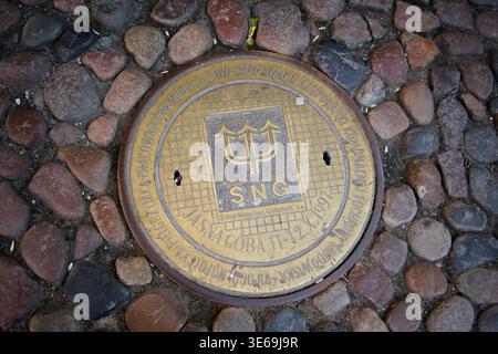 Decorative manhole cover of Saur Neptun Gdańsk water utility with trident logo on cobblestones, Poland Stock Photo