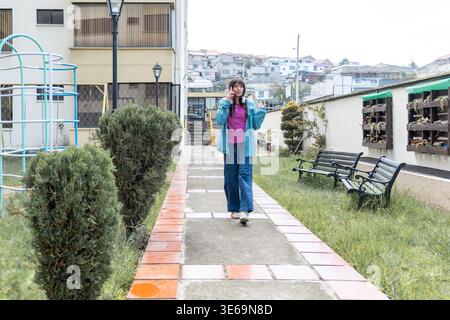 Woman walking on a sidewalk, talking on her mobile phone in an urban residential area Stock Photo