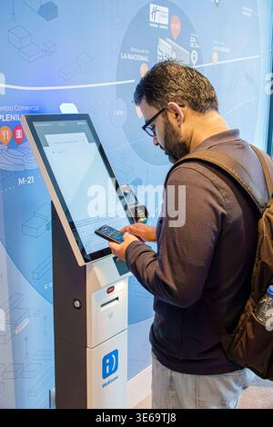 Madrid Spain,Holiday Inn Express IHG hotel,inside interior,man male adult using touchscreen kiosk checking information smartphone backpack traveler se Stock Photo