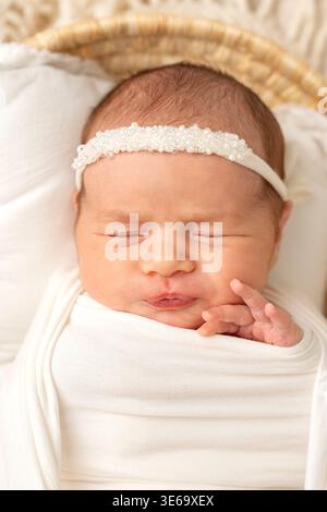 Portrait of a sleeping newborn baby wrapped in soft white fabric. Minimal newborn photography with gentle light, calm expression and cozy atmosphere Stock Photo