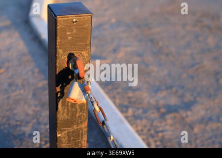 Rusty padlock on a metal chain secured to a post at sunset. Close-up view with text space. Security measures, outdoor protection, and the weathered te Stock Photo