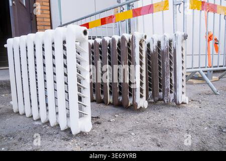 Cast iron radiators placed on construction ground beside safety barrier, showing building renovation, heating system replacement, and site workflow Stock Photo